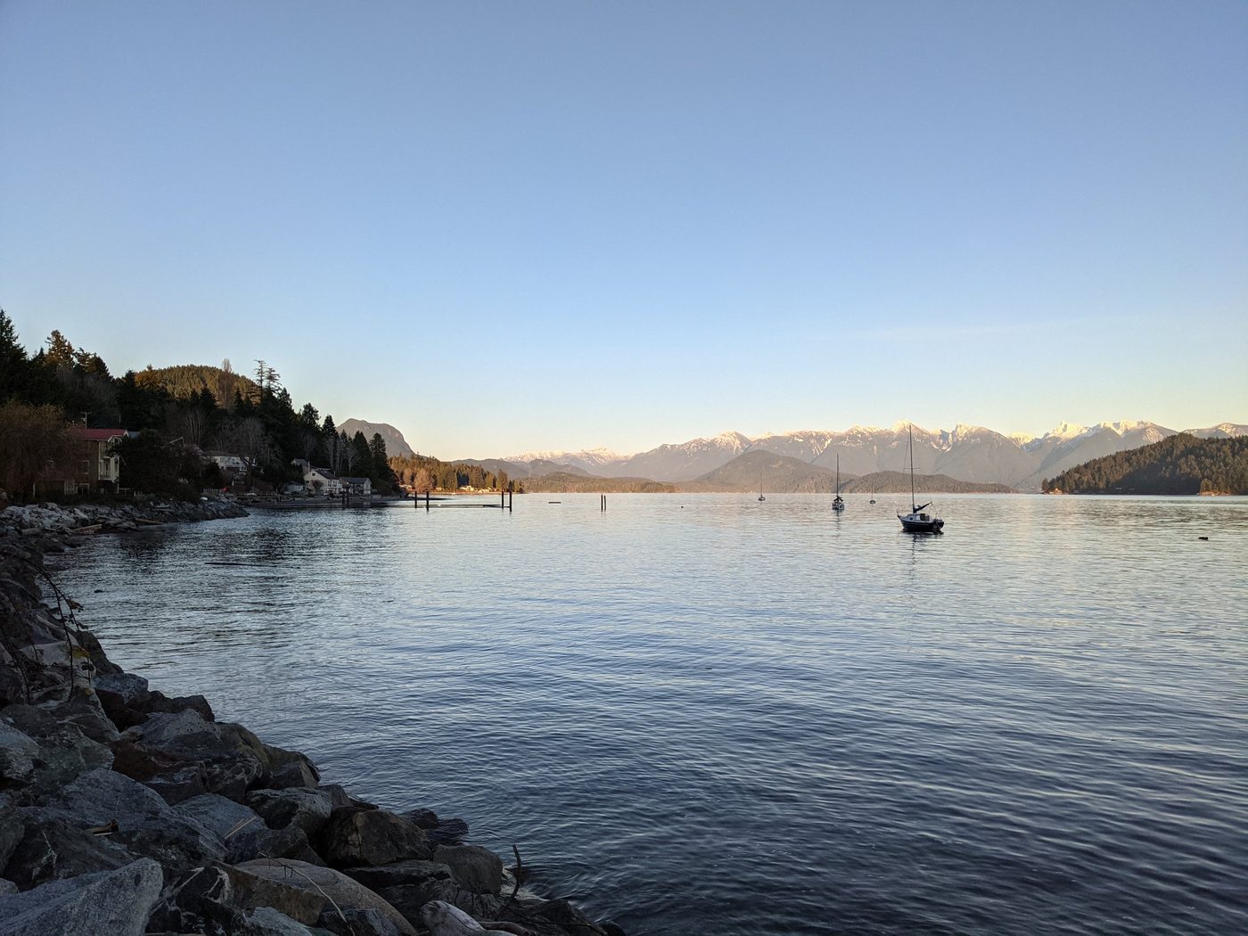 Gibsons harbour at dusk, with sailboats at anchor and snow-capped mountains beyond